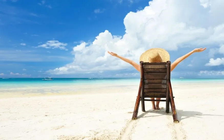 A woman in a sun hat, sitting in a fold-out lounge chair at the beach.